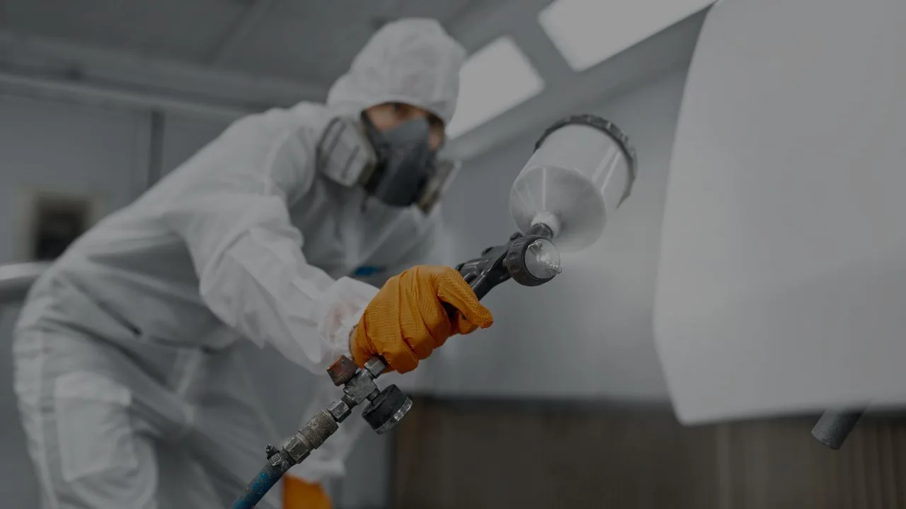 Técnico aplicando pintura a una pieza en un taller de pintura automotriz